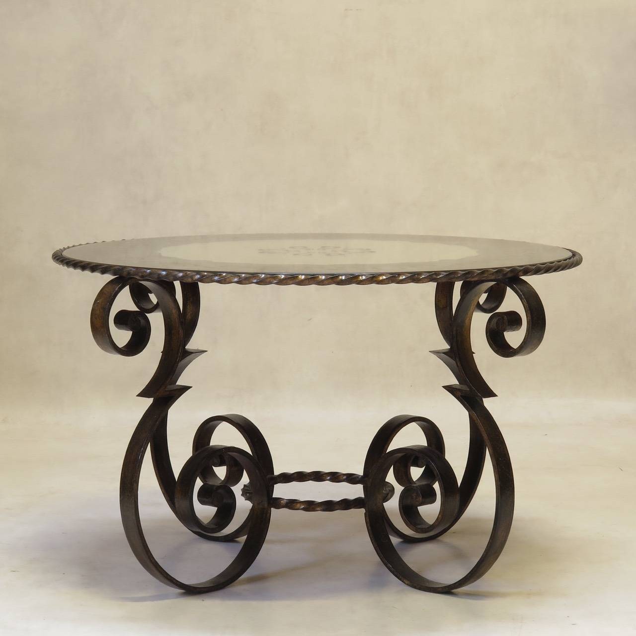 Delightful and chic round coffee table with a heavily scrolled wrought iron base with zig-zag detail and twisted gilt iron stretcher and table top surround. Gilded base. Eglomisé mirrored table top.