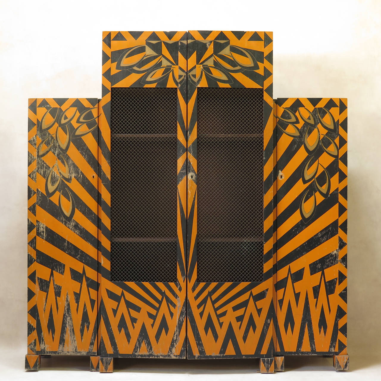 Fun, unusual and very decorative set comprised of a bookcase, a table, two armchairs and a pedestal, painted in a cubist motif in orange, black and gold paint. 

The armoire has three sections: two side doors containing shelves, and a higher