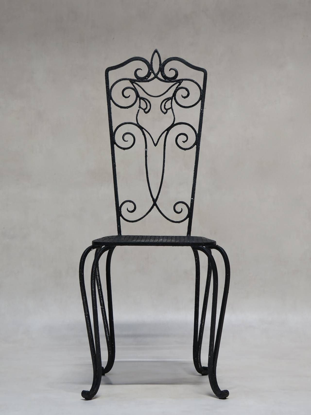 French wrought-iron outdoor dining set comprised of a rectangular table and four chairs.

The table is comfortably large, with a cloverleaf-patterned sheet metal top, raised on cabriole legs with scrolled feet, and a twisted iron X-shape