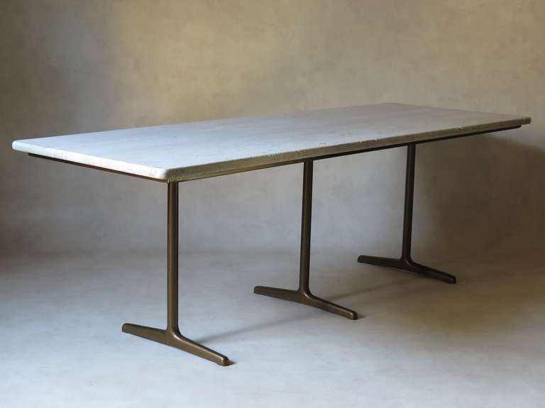 A long and elegant table with simple lines and a beautiful antique stone top supported by a bronze-coloured cast iron base with three central legs.