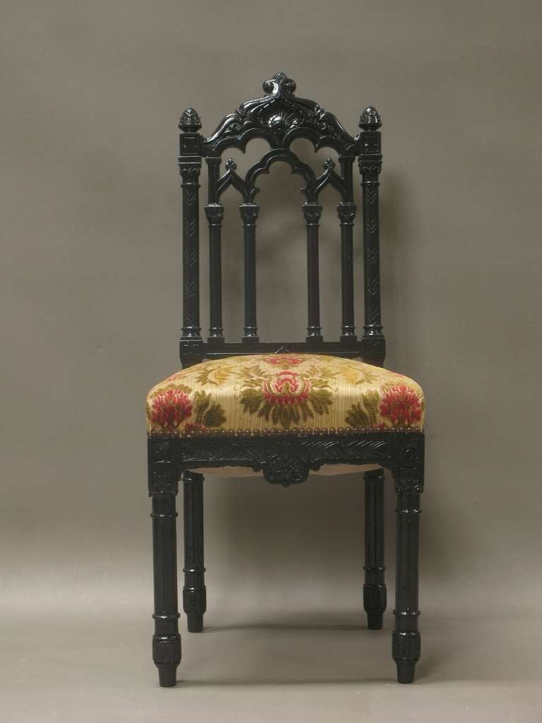 Six gothic revival chairs, with elaborately carved and engraved backs, aprons and legs. Painted black. Original upholstery with a velvet floral design.