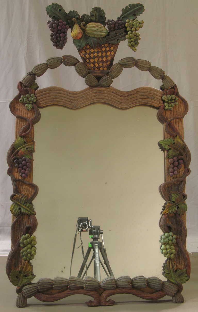 Very charming mirror with carved frame. The surround is carved with vines and and two serpents. The top is mounted with a colourful fruit basket. Original mirror.