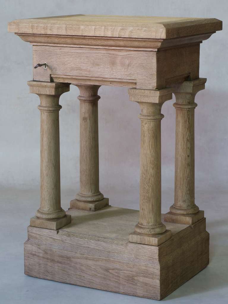 A brushed oak side table / pedestal / plant stand. The top supported by turned columns. The front apron opens, forming a drawer, with original hardware.
