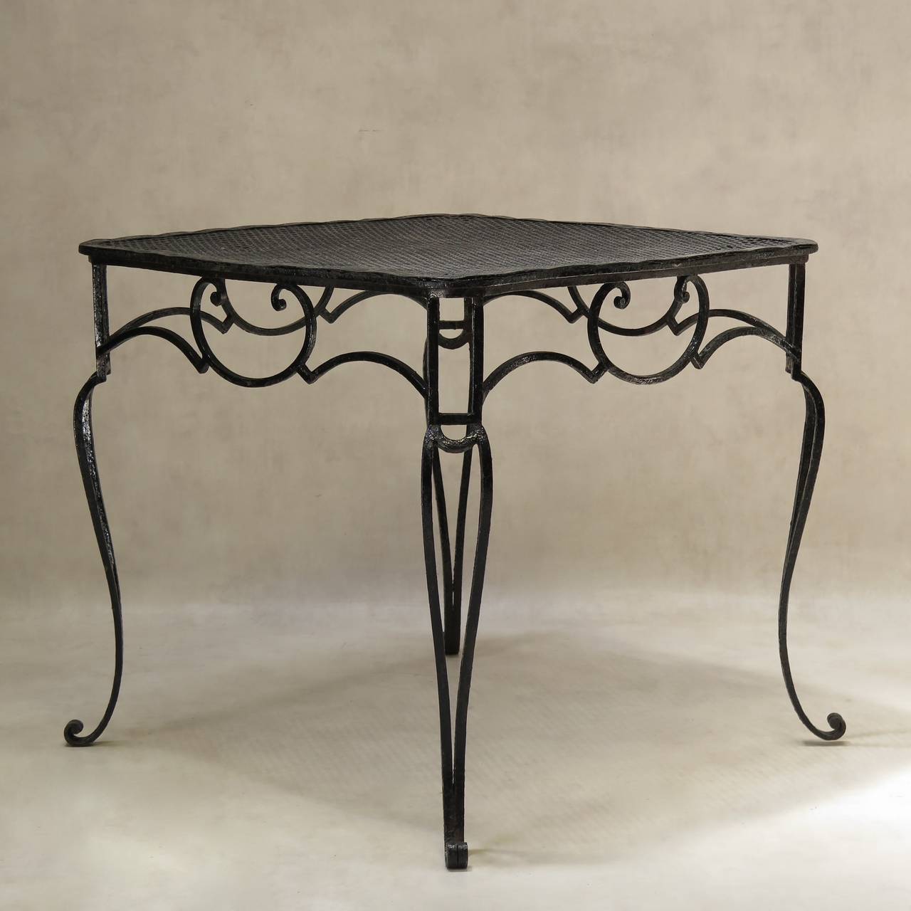 Elegant wrought-iron dining table of baroque inspiration. The square top has serpentine edges and is made of perforated sheet metal. Shapely apron and cabriole legs ending in scrolled feet. Original glossy black paint. Works well indoors or