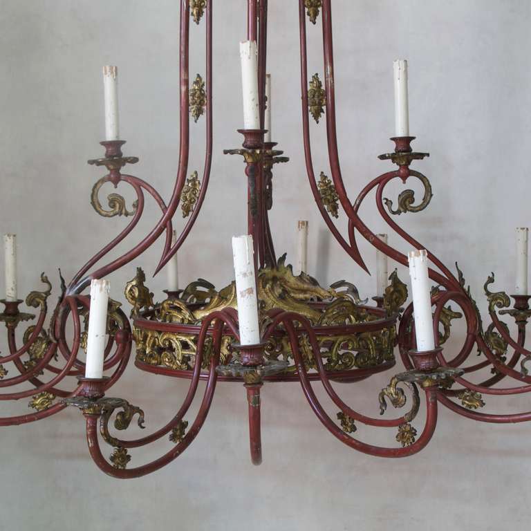 Large sixteen-light converted gas chandelier, with two tiers of lighting. 
Elegant sweeping lines and arabesques.
Tubular metal structure, with original deep red paint, and gilt metal Rococo decor.