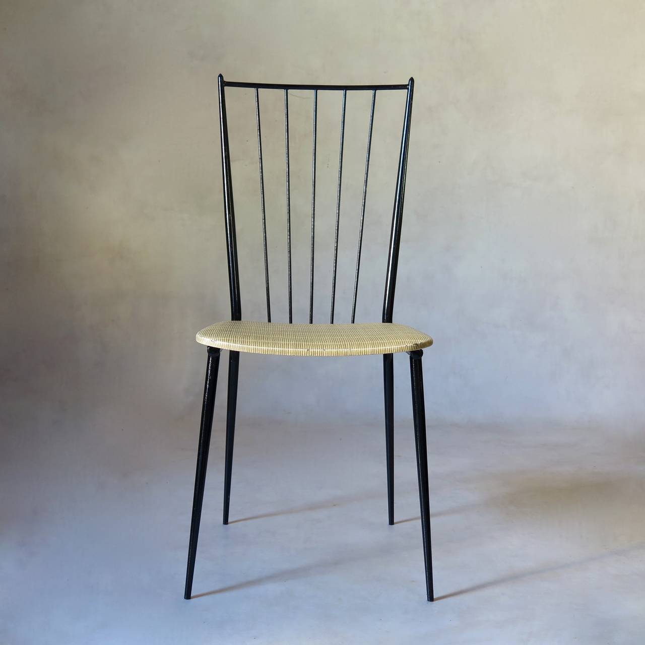 Set of six chairs in the style of French Mid-Century designer Colette Gueden. Tubular iron structure with black lacquered finish. The seats are upholstered in textured faux-straw vinyl.