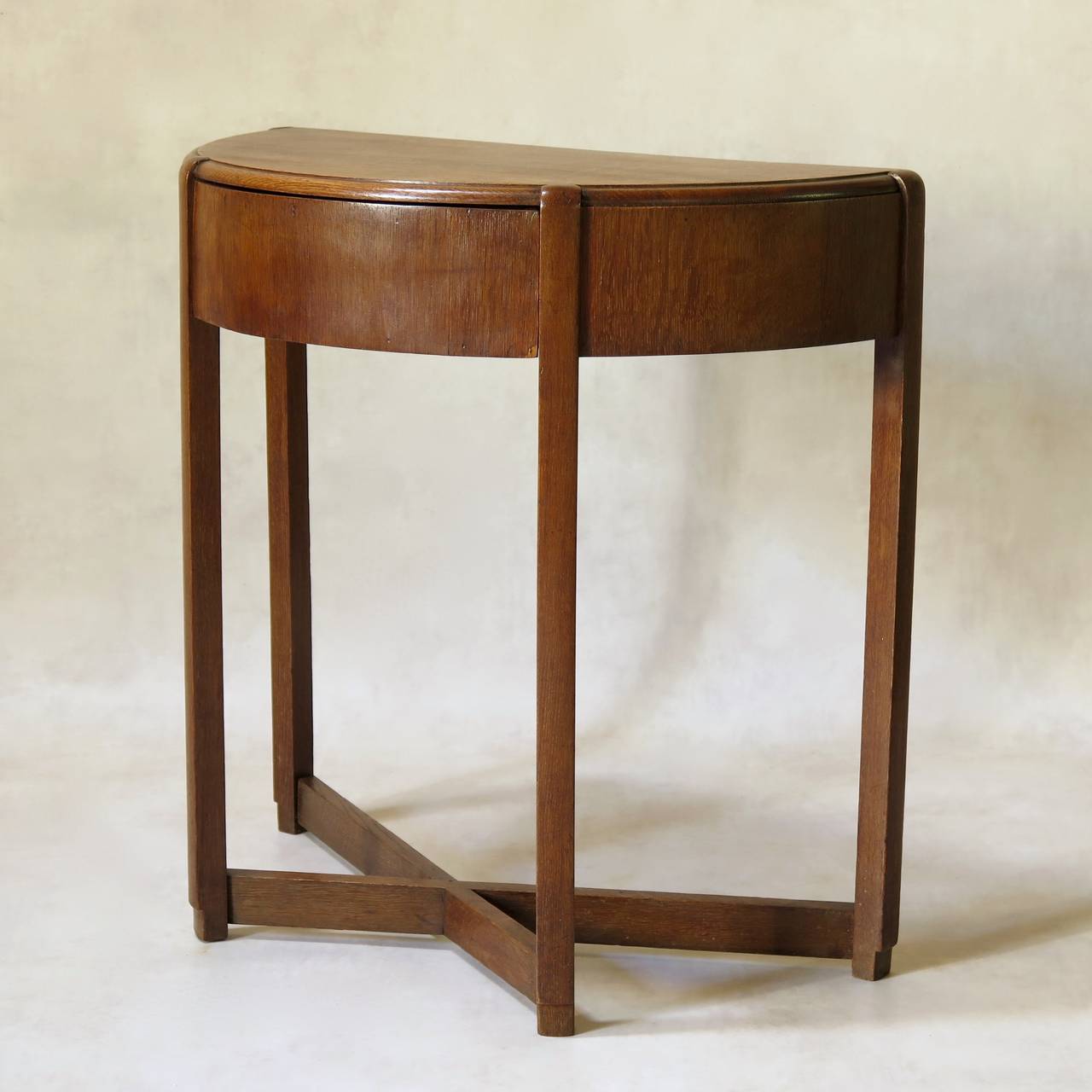 Chic 1940s demi-lune console of appealing, minimalist design. The legs, in solid oak, are joined by an X-shape stretcher. The apron is faced in oak veneer, and has a central drawer.