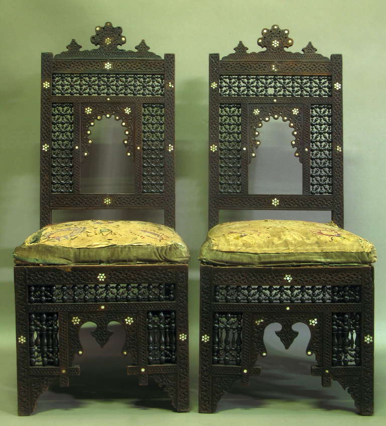 Pair of elaborately carved and decorated chairs, possibly from Syria, with moucharabieh design, and inlaid with mother of pearl. Original velvet and embroidered cotton seats.