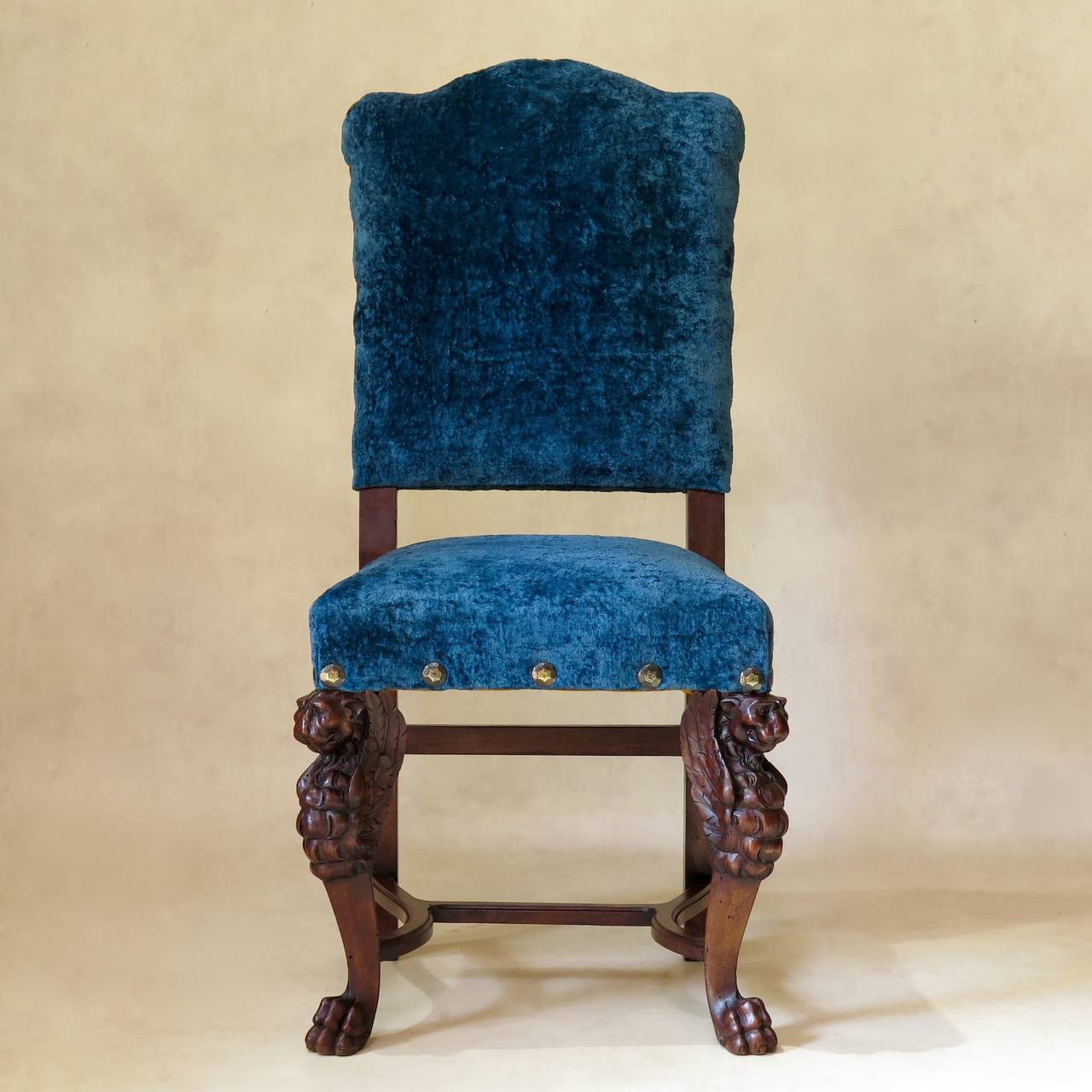 Set of four Renaissance style chairs with dramatic, carved lion head legs, ending in paw feet. Newly re-upholstered in a vintage, deep blue crushed velvet, with large nail head trim.