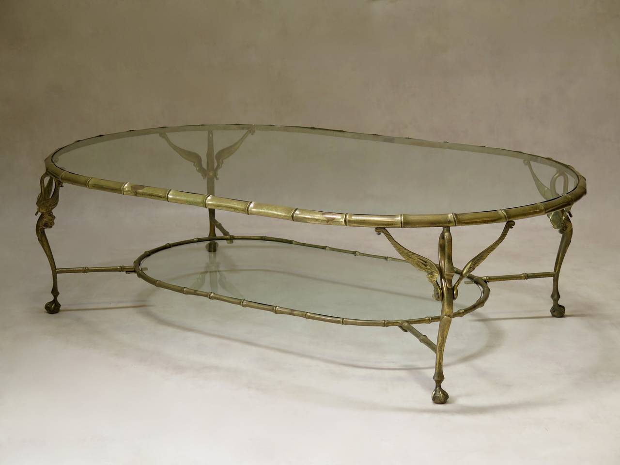 Chic set of five solid brass coffee tables with glass tops. Decorated with elegant swan heads at the top of each leg and ending in claw and ball feet. The glass tops are set inside faux-bamboo surrounds.
One table is a large oblong shape with a