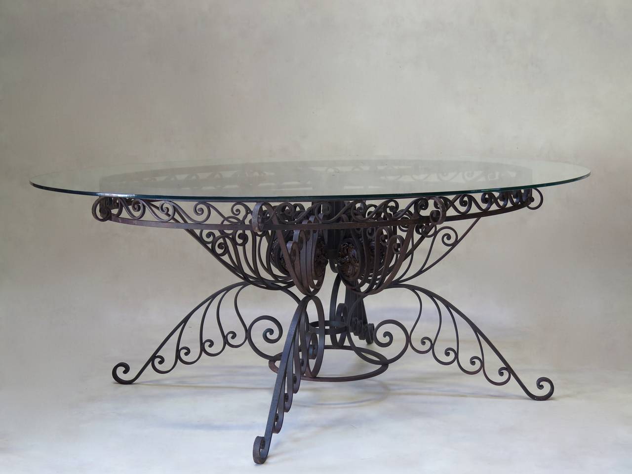 Stunning oval wrought iron dining table with an elaborately scrolled base, adorned with flower rosettes. Beautiful craftsmanship and design. Fitted with an oval glass top.
