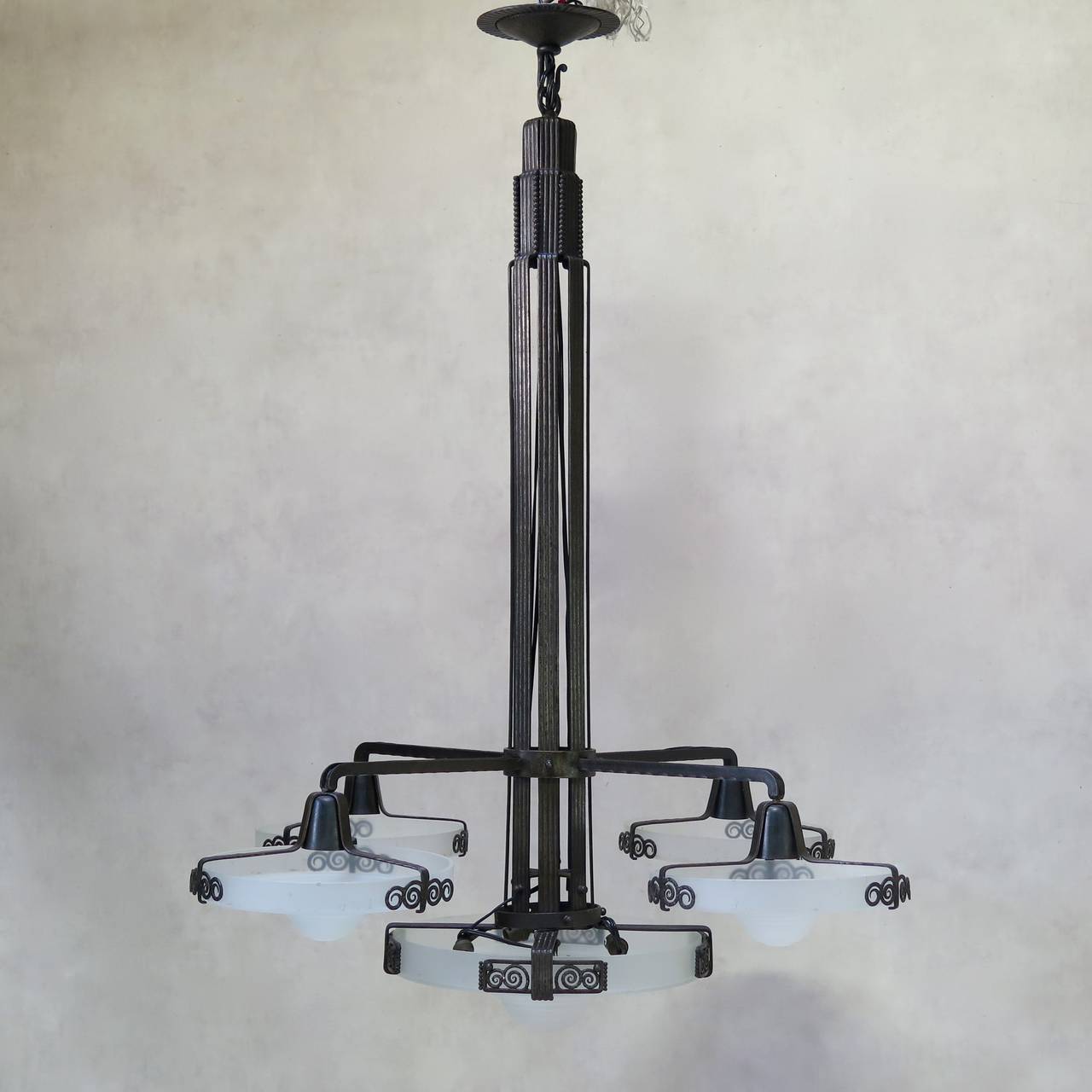 Large-scale chandelier with a wrought-iron structure and five large, round, stepped, frosted glass shades (a large central one and four slightly smaller, satellite ones).

Well made, with elegant details: the canopy has a ridged trim and