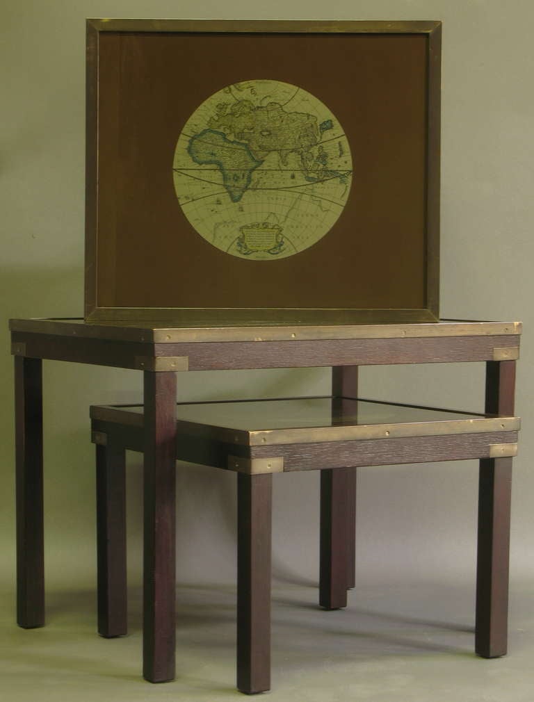 Three rectangular nesting tables, of dark wood with brass hardware, and glass tops, with antique style world atlases beneath on brown paper backgrounds.

Dimensions provided below are for the largest of the tables. The smallest table is square.