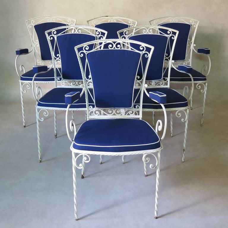 Chic set of six wrought-iron chairs with twisted and curlicue detailing. Generously scrolled arms. 
Raised seats, backs and armrests, upholstered in dark blue canvas with white piping. 
Perfect for outdoor use.