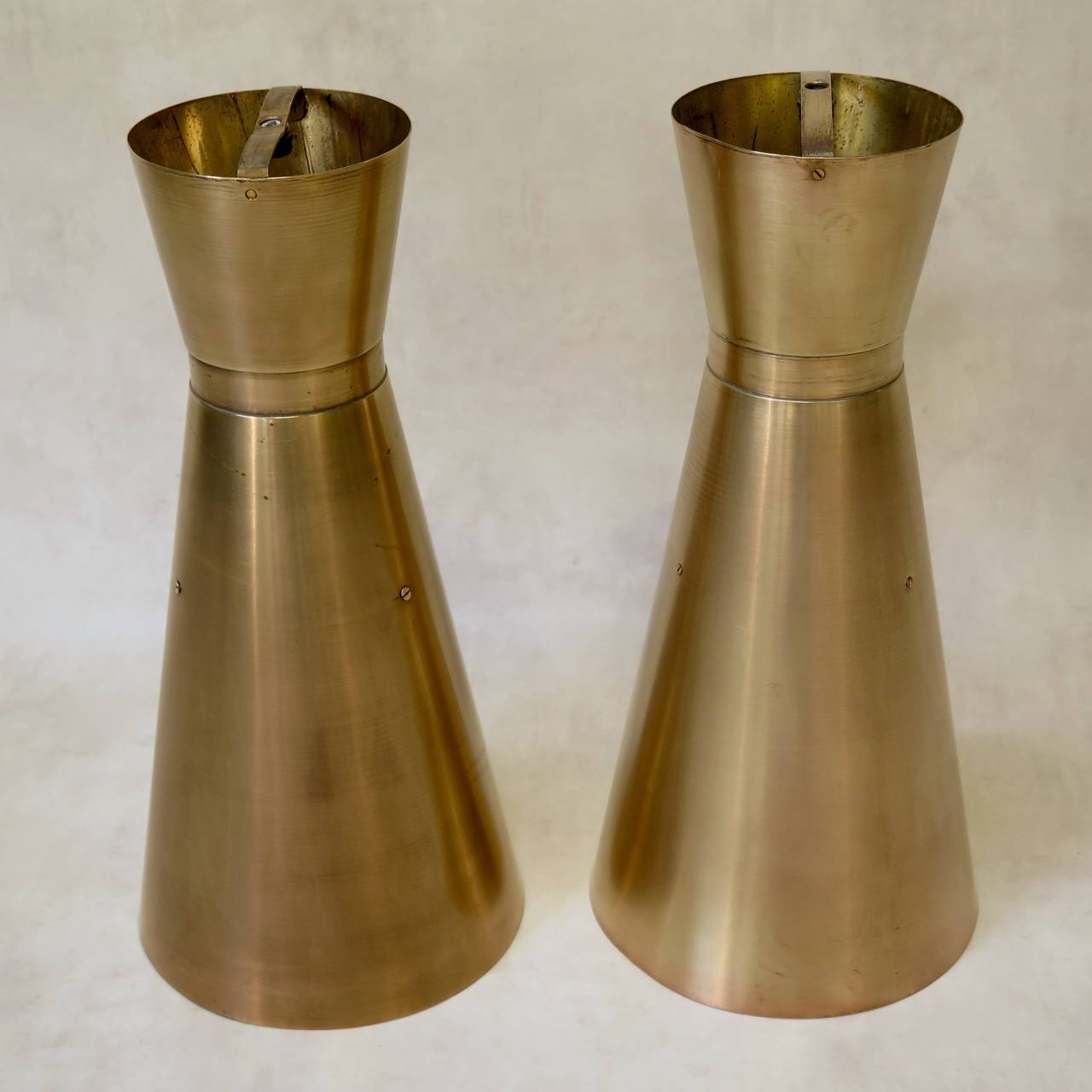 Elegant and sleek set of seven heavy, solid brass hanging lights of conical shape. Two sockets inside for uplight and downlight. Very well made.

The diameter provided below corresponds to the larger end. The smaller top end has a diameter of 15.5