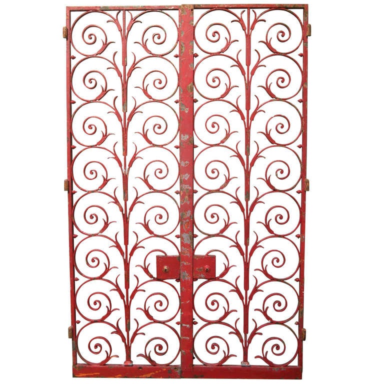 Very heavy and well-made pair of hinged wrought iron grilles or gates, painted red, with orange colored primer paint visible beneath in small areas. Elegant symmetrical scrolling arabesque design. Two pairs available.

There is a difference in width