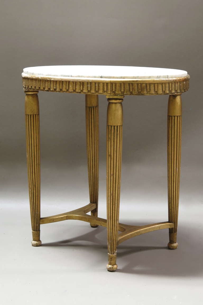 Elegant and lovely gilt Art Deco period side table with carved apron, reeded and and fluted legs and small round bun feet. Raised marble top, white with grey/green veins.