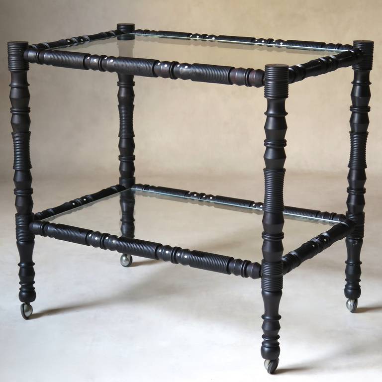 A very finely turned ebony side table or bar cart on wheels, with bone inlays and two glass tiers.