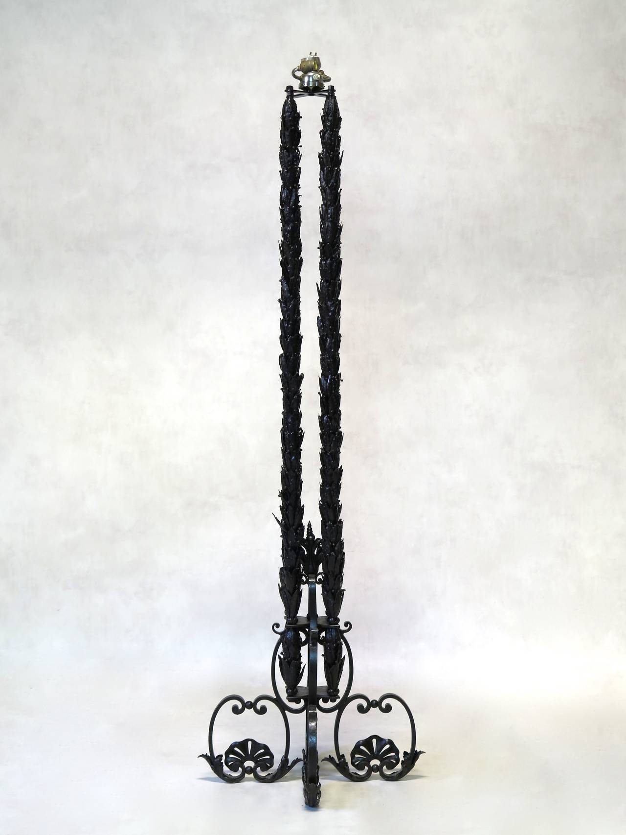 Preciosa lámpara de pie de hierro forjado de la década de 1940. El tallo está formado por cuatro columnas de intrincadas coronas de hojas de laurel, sostenidas por una elegante base de volutas con detalles de hojas de acanto y rosetas en forma de