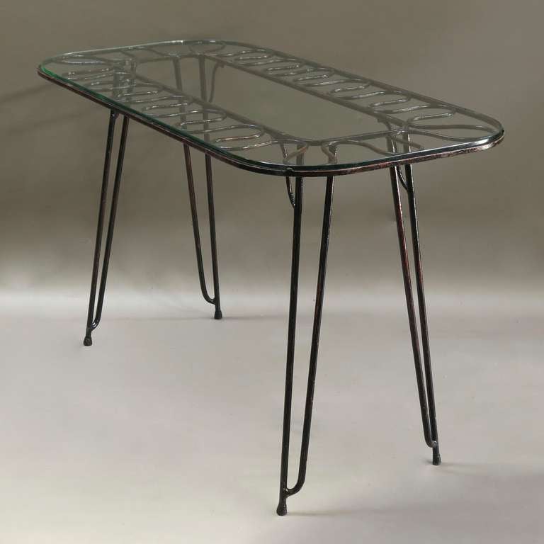 Lovely wrought iron console table, with several coats of colorful (red, green) paint visible beneath the glossy black. 

Top with a frieze of undulating motif and rounded edges. Glass top.

Splayed legs.