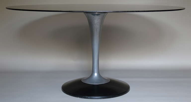 Oval dining/center table with a smoked glass top and tulip-shaped base of cast aluminum and black moulded plastic.