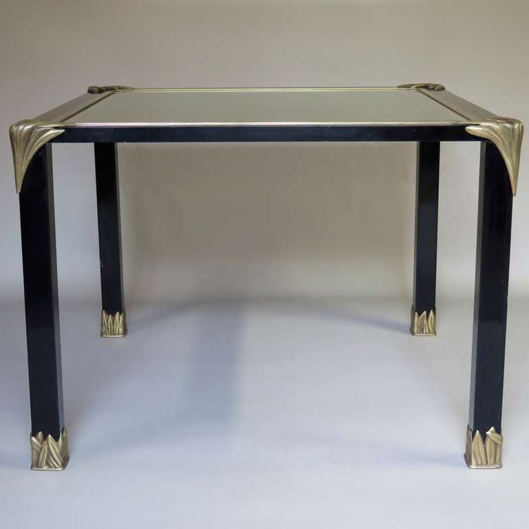 Chic and elegant square center / games / dining table.

Metal structure lacquered black. The feet and corners of the table are decorated with brass leaf motifs. 

The table top is a beveled mirror (original, with slight sugaring) with a brass