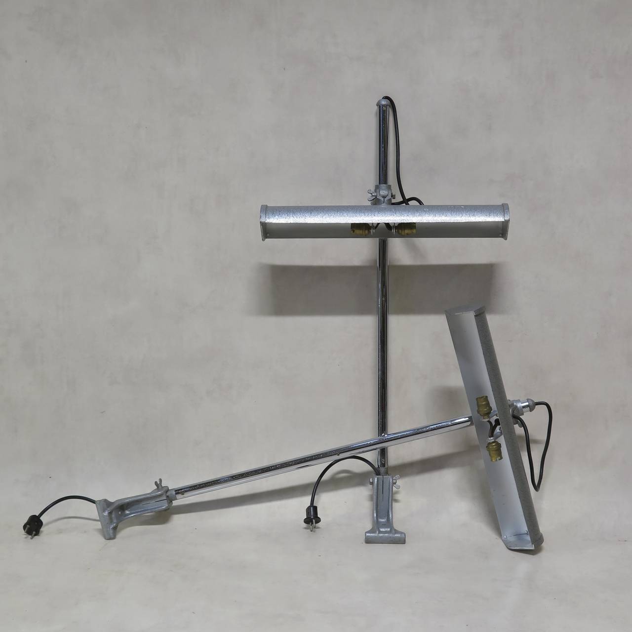 Pair of desk lamps with adjustable shades (height and angle), designed to be fixed to the edge of the table or work surface. The stems are chromed and the shades are painted in silver Industrial-quality hammer paint.