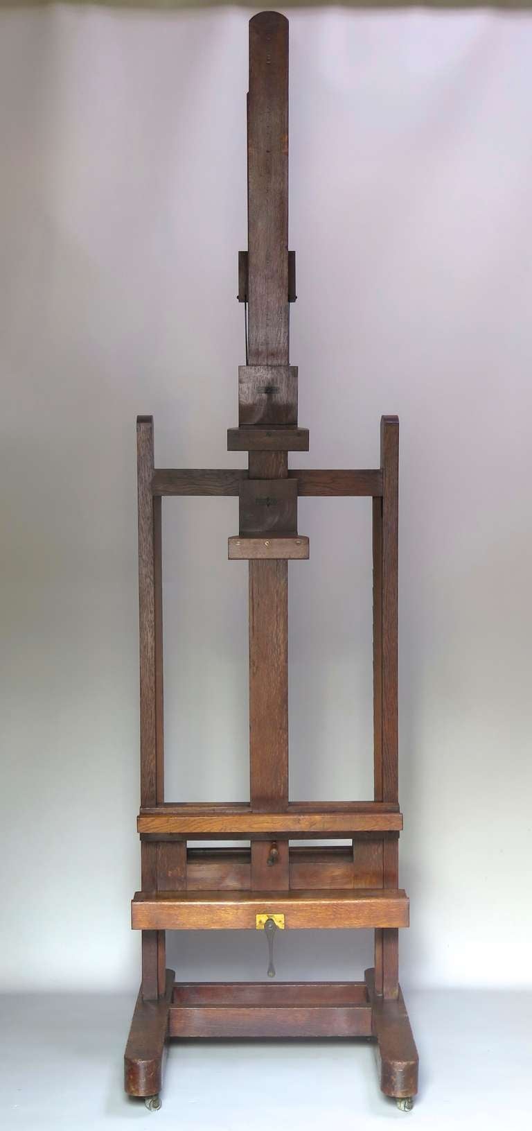 An oak double-sided artist's easel with adjustable height and adjustable angle rests, on an H-shaped frame. On casters.