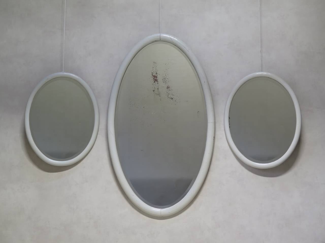 A set of oval mirrors, two smaller ones and one large. The frames are wood, painted glossy white. Original beveled mirrors, with some slight sugaring, especially on the larger one.

Dimensions provided below are for the larger mirror. The small