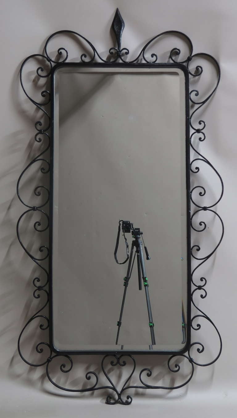 Tall beveled mirror with rounded edges set in an elegant wrought-iron frame.