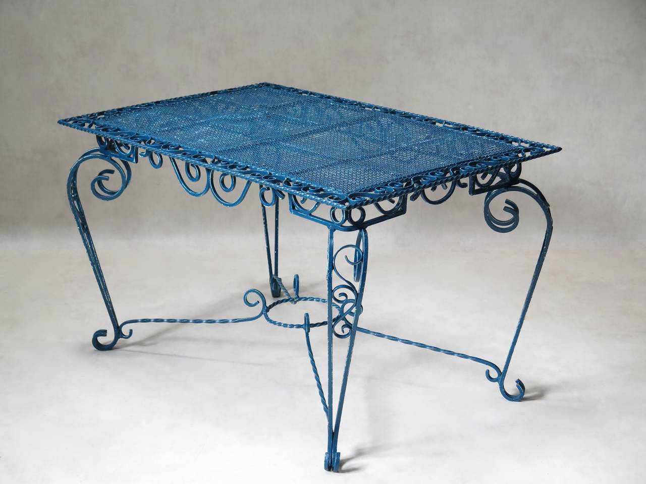 Outdoor dining set comprised of a rectangular table and four armchairs of solid wrought iron with elaborate scrolling curlicue motifs.

The tabletop as well as the chair backs and seats are made of cloverleaf-patterned sheet metal, in very good
