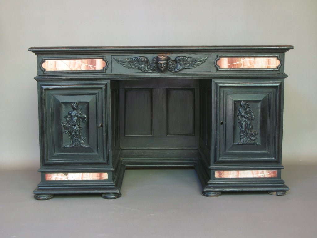 Ebonized desk with compartments on either side. Central drawer decorated with a cherub. Marble inlay. Leather top.