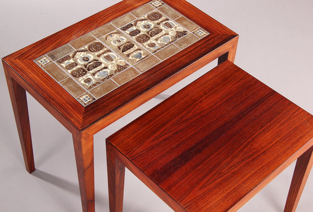 A set of two nesting tables with inlaid stoneware tiles by Nils Thorsen for Royal Copenhagen. Produced by Haslev Møbelsnedkeri.