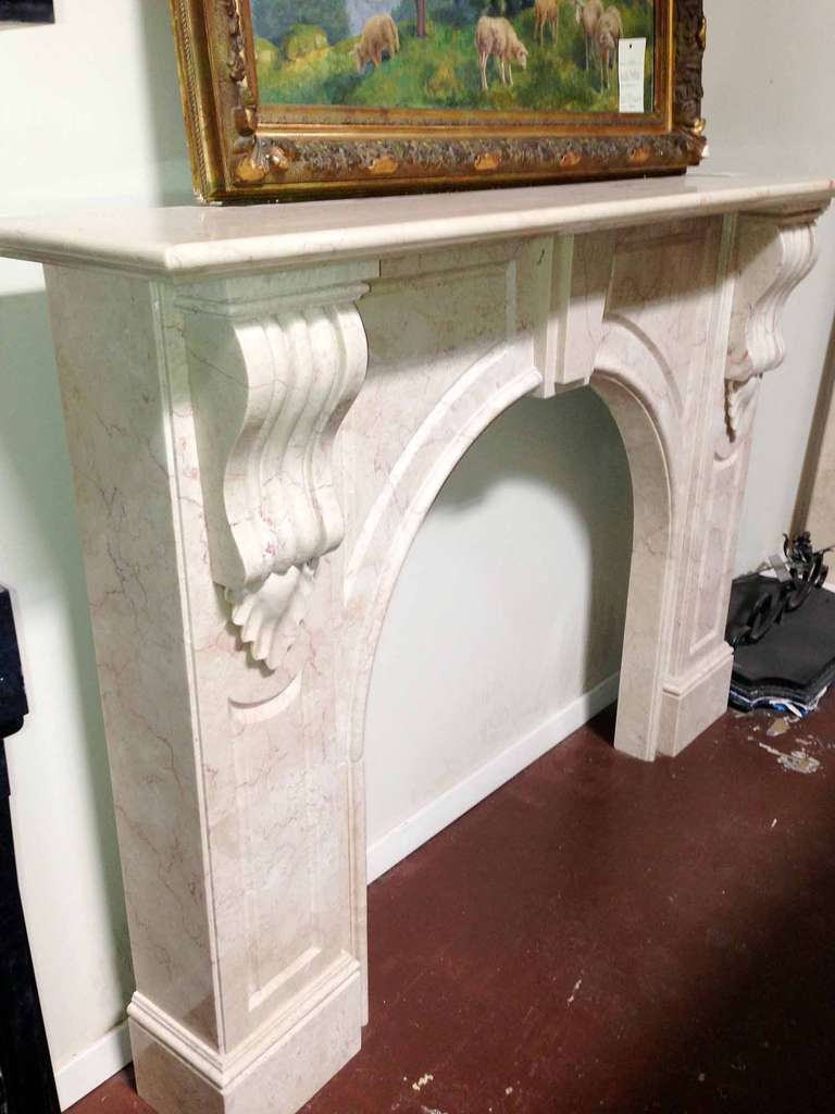 This antique marble mantel is beige with violet veins and features an arched firebox opening.