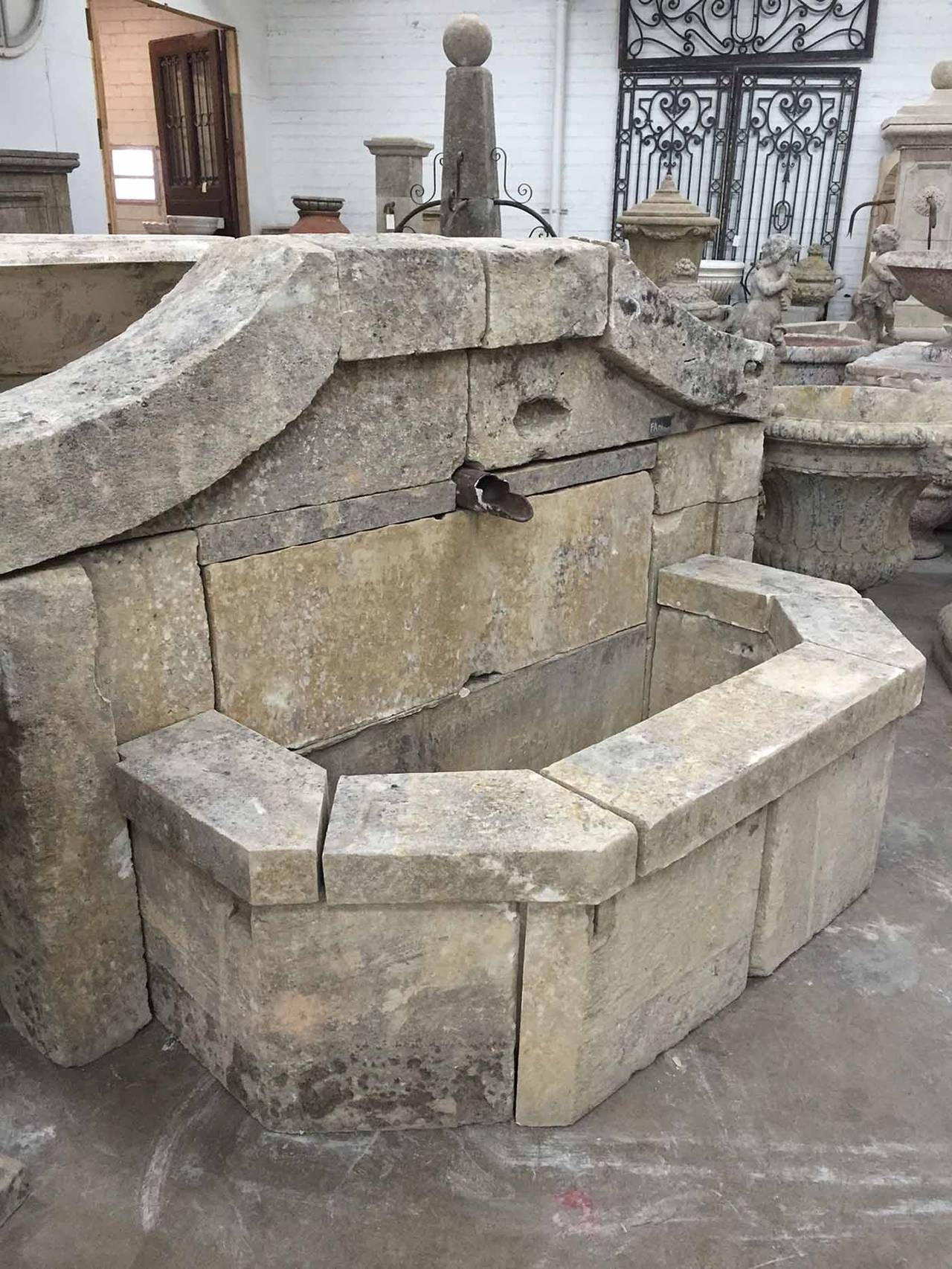 This fountain, composed of 18th/19th century stone, has a semi-octagonal wall and a large single water spout.