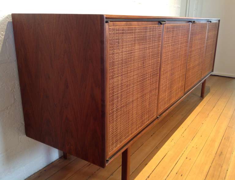For your consideration, a early Florence Knoll walnut credenza from the 1950s.  Four doors with leather pulls and cane fronts. 
Two center doors open to reveal two drawers, with each end door having one shelf.