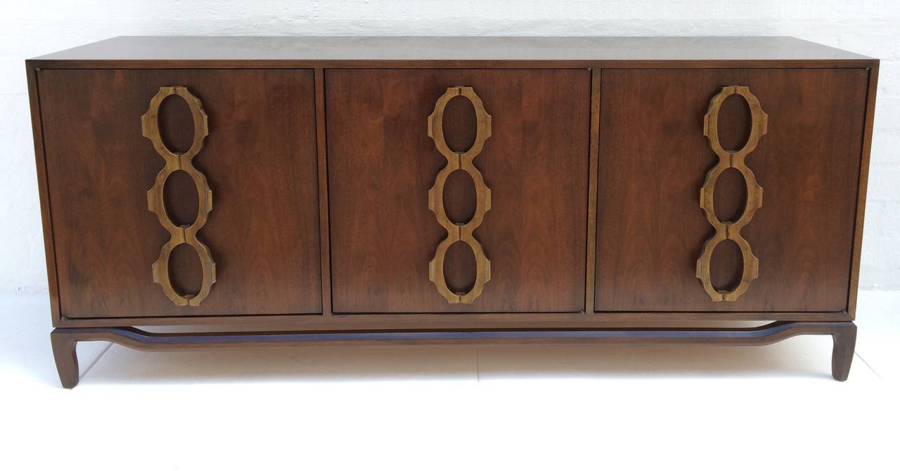 This beautiful credenza has three doors with aesthetically pleasing pulls. 
Two doors open to reveal an adjustable shelf, with the other door revealing three drawers. 
 The wood is solid and appears to be walnut with a high gloss finish. 
Marked