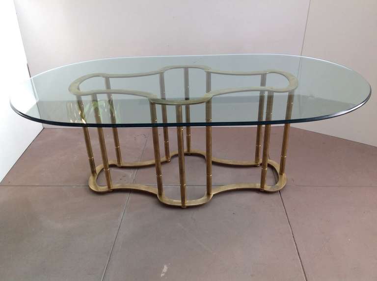 A antique brass dining table designed by Mastercraft with a 3/4 inch thick oval glass top that is 84
