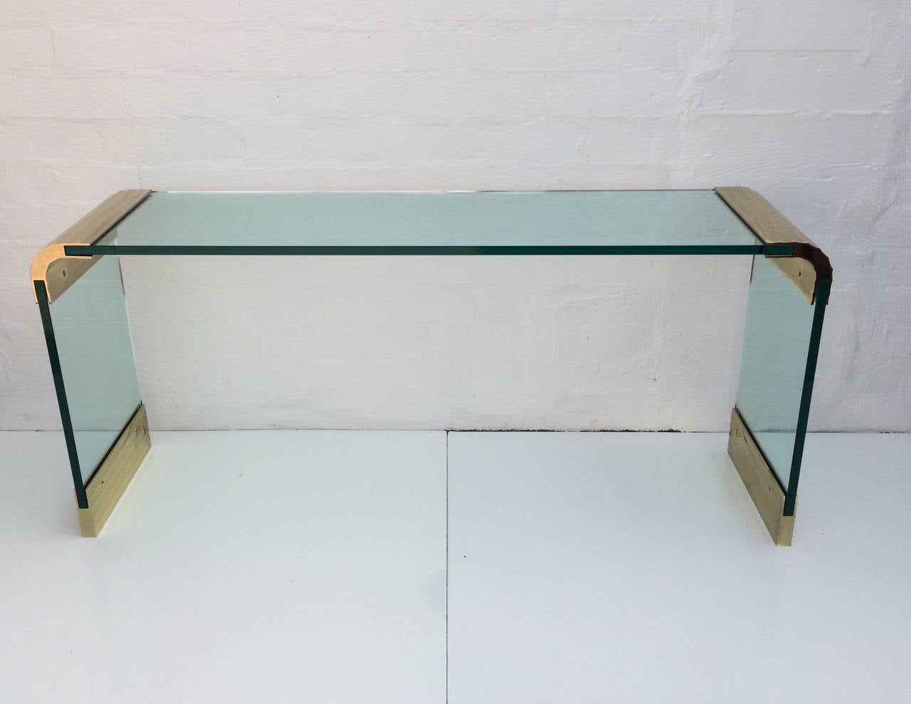 Brass and glass waterfall console table designed by Leon Rosen for Pace Collection.
This table consist of three pieces of 3/4 inch thick glass held together by polished scalloped brass end pieces and with polished scalloped brass feet.
circa 1970s.
