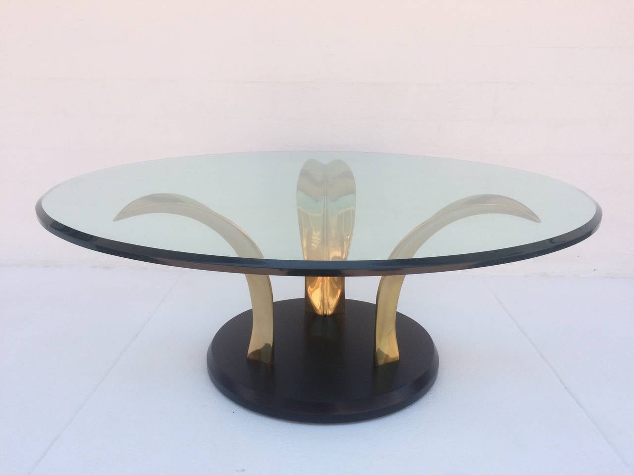 1970s polished brass and glass coffee or cocktail table. 
Consist of a black laquer base that has three polished brass leafs that support a 40.5
