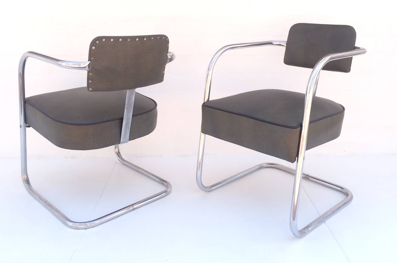 A pair of 1930s chrome and upholsterd chairs designed by Kem Weber.   
Newly reupholster in a faux shagreen leather with black leather piping.