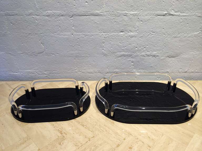 A pair of display trays, one large and one smaller in the style of Dorothy Thrope for Grainware circa 1970s
Both trays consist of black acrylic bottoms with four clear acrylic handles that inset into nickel that attaches to the bottoms making a