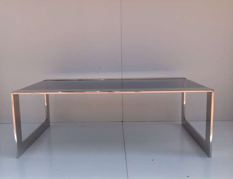 A solid polished stainless steel base with a new smoked inset glass top coffee/cocktail table by Brueton.