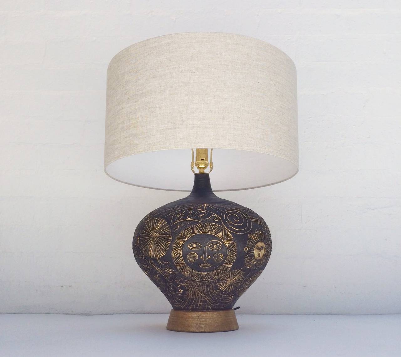 A 1950s plaster table lamp hand-painted black with gold leaf.
This lamp has sun face images.
All new brass hardware and newly rewired.
New oatmeal linen shade.