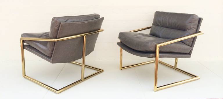 A pair of heavy tubular brass lounge chairs newly reupholstered in a distress gray leather.