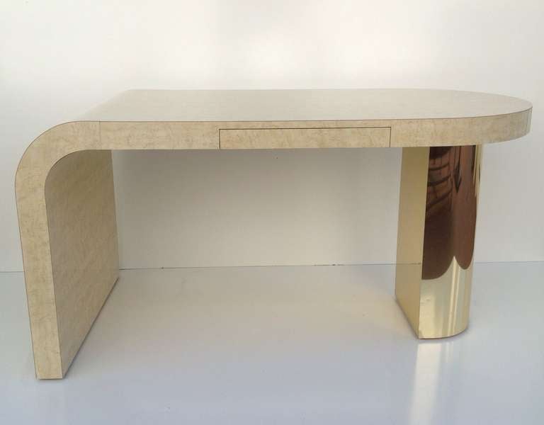 This desk designed by Milo Baughman for Thayer Coggin is from the 1980s.
It is formica with a bleached burl wood design.
The support leg is covered in a thin brass and it has one drawer.