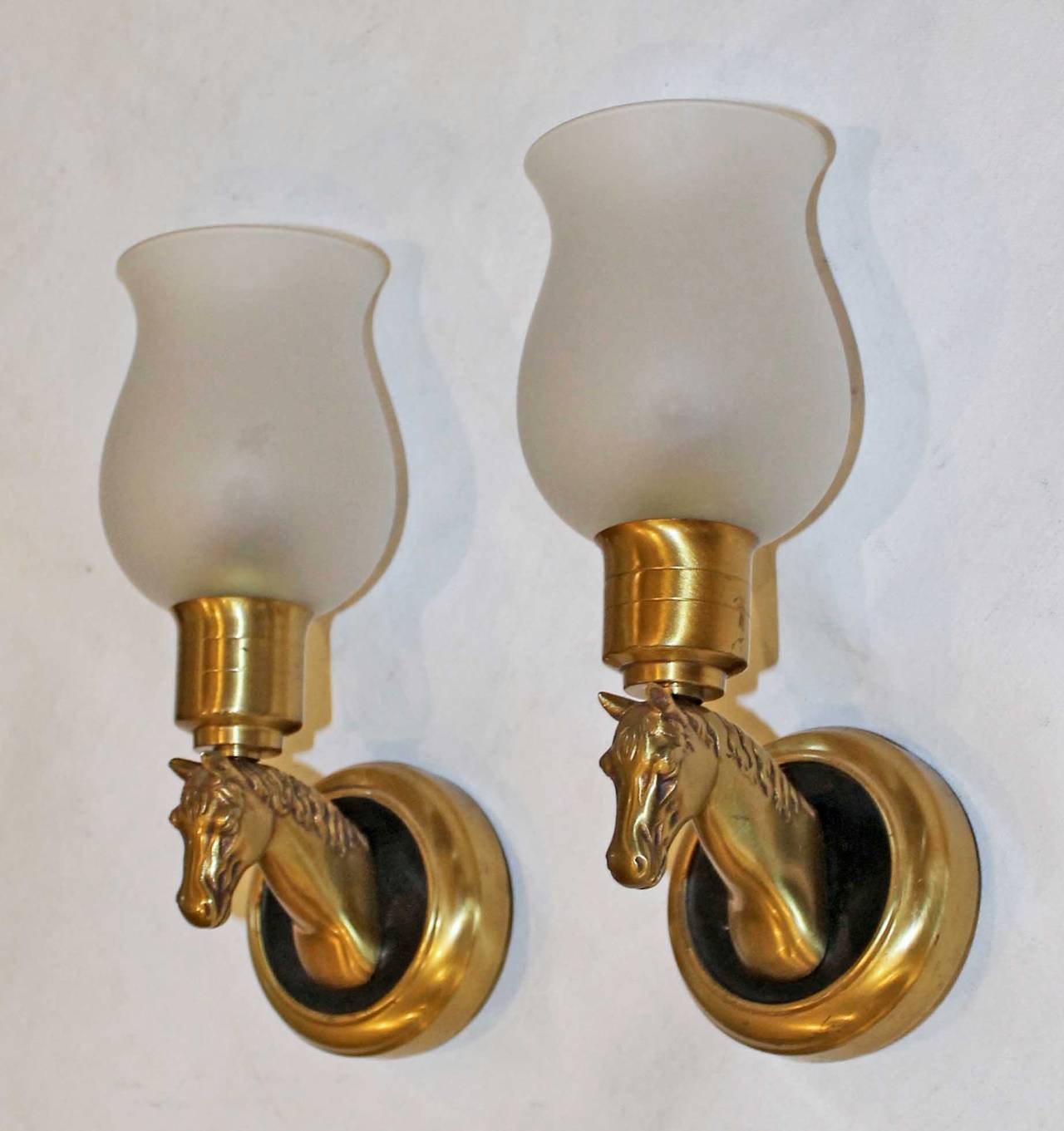 Pair of dimunitive polished and darkened brass horse wall sconces with matte glass shades. Rewired. Each sconce uses 1 - 40 watt max candelabra base bulbs.