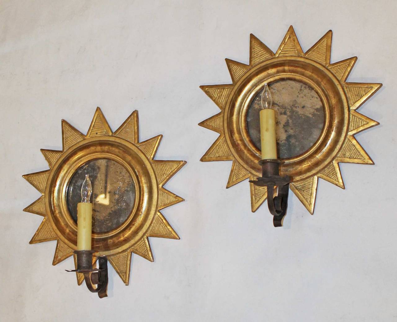 A rare and beautiful pair of sunburst soliel giltwood Directoire style wall sconces, late 19th Century. The 24k water gilt finish is exquisitely applied, the mirror backs having the patina of age. Originally candle sconces with hand forged iron
