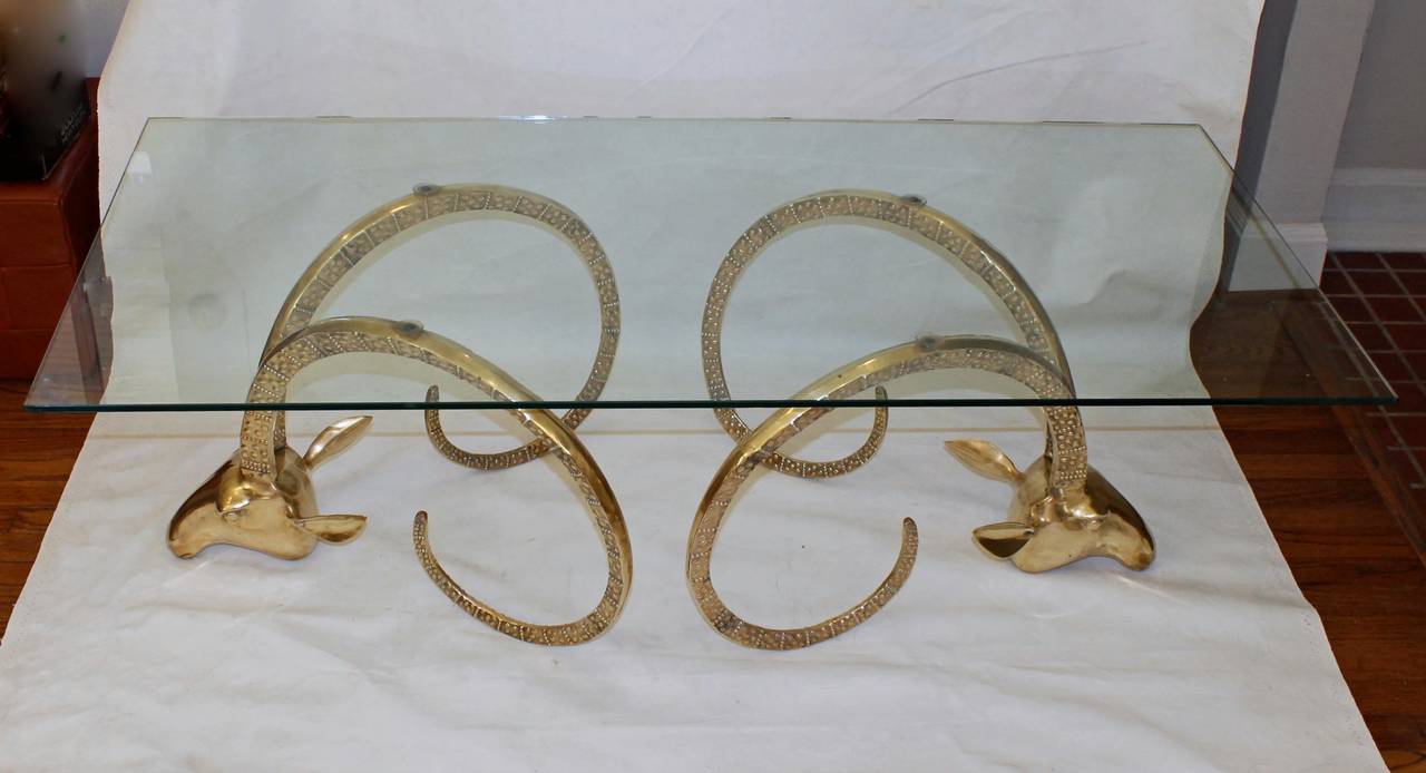 Beautifully sculpted brass ibex head coffee table with rectangle glass top, in the style of Chervet. Each brass base measures 17