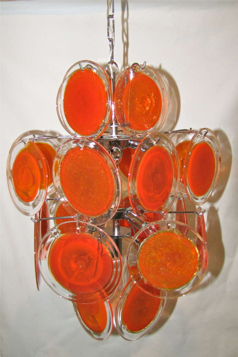 Vistosi hand blown orange glass disc 9 light chandelier with chrome frame, the glass discs alternate in 2 styles as seen in close up images. Uses 9 40-watt candelabra size bulbs. Rewired. 
Size: 23